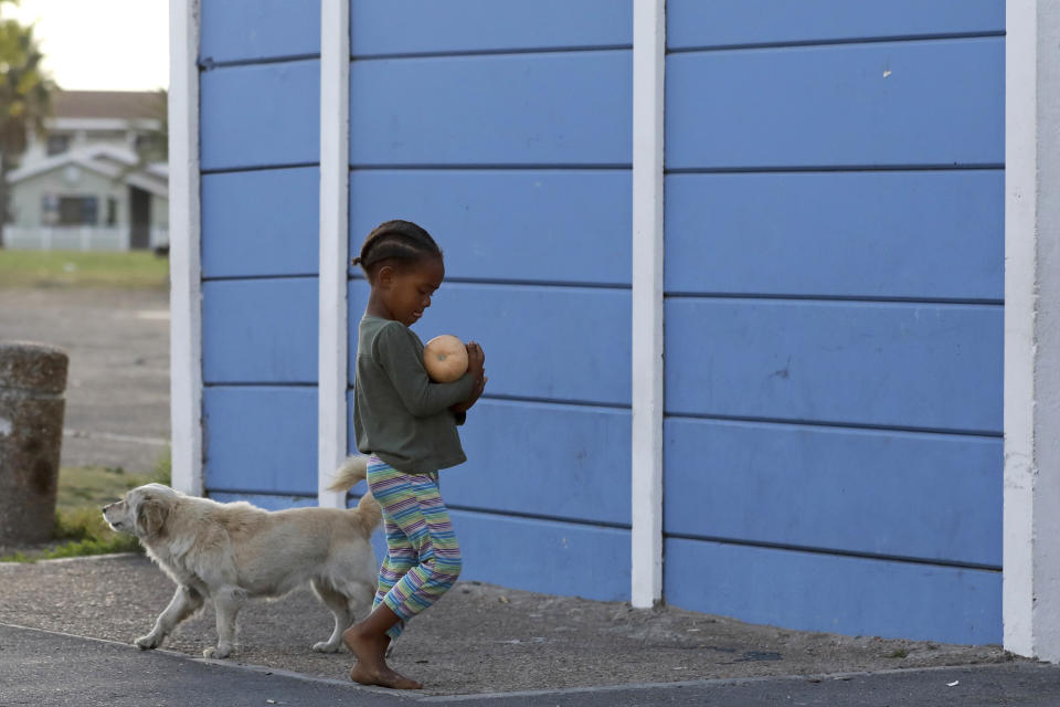 In this May 2, 2020, photo, a child walks with a butternut squash in the Manenberg neighborhood of Cape Town, South Africa. A preacher recruited members of street gangs to distribute food in a violent and poor neighborhood during the coronavirus lockdown. (AP Photo/Nardus Engelbrecht)