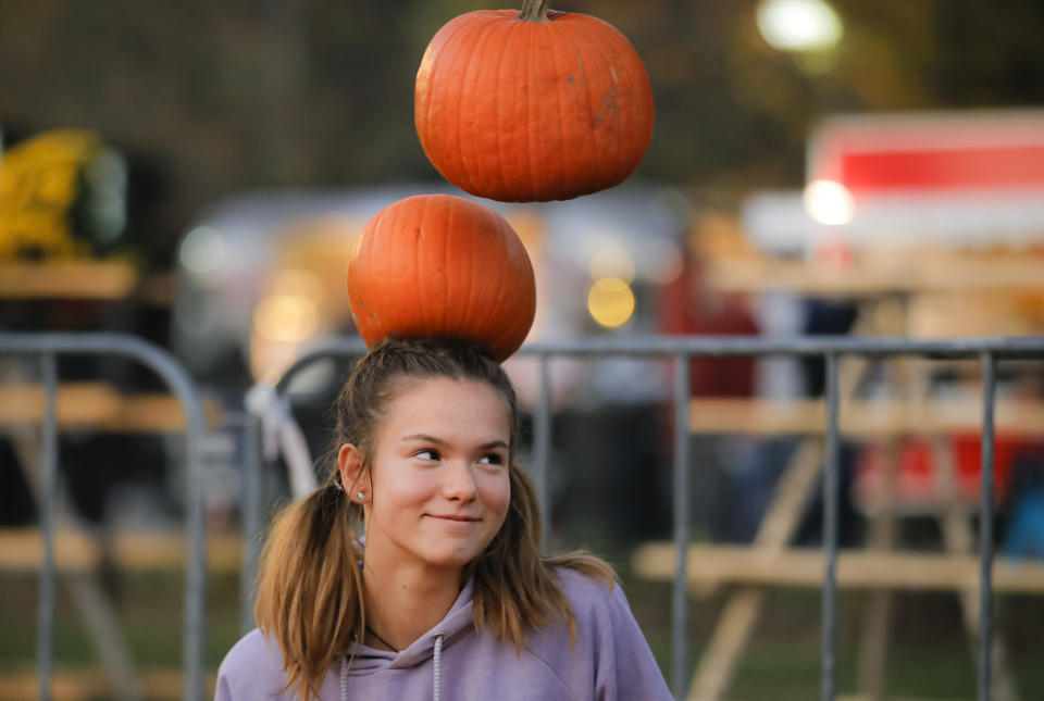 In this Friday, Oct. 25, 2019 photo a girl tries to balance pumpkins on her head at The Halloween Pumpkin Fest in Bucharest, Romania. (AP Photo/Vadim Ghirda)