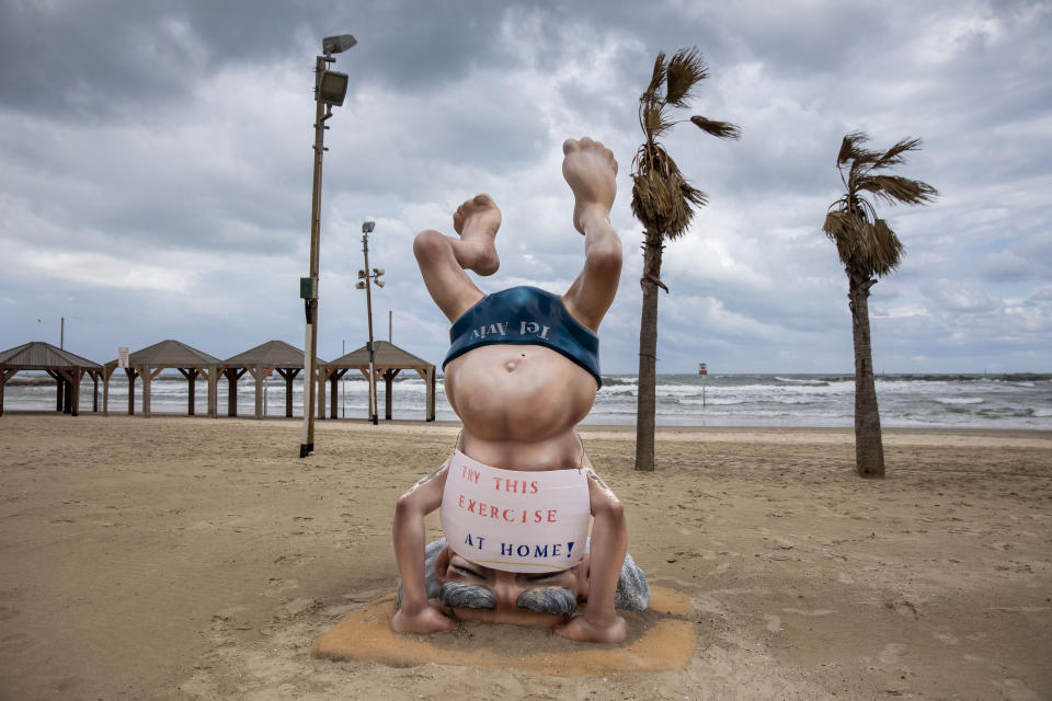 A sign calling people to stay home to reduce the spread of the new coronavirus is placed on a statue of the first Israeli Prime Minister David Ben Gurion at a beach in Tel Aviv, Israel, Friday, March 20, 2020. Prime Minister Benjamin Netanyahu said he was further tightening restrictions on movement, with exceptions only to go out for food or other urgent matters. For most people, the new coronavirus causes only mild or moderate symptoms. For some it can cause more severe illness. (AP Photo/Oded Balilty)