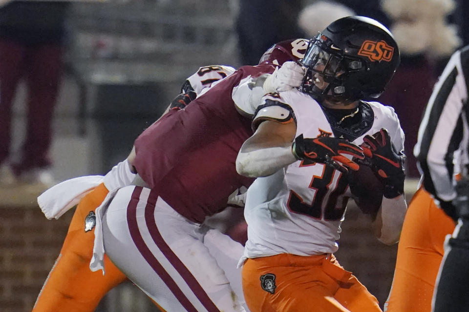 Oklahoma defensive end Ronnie Perkins, left, grabs the face mask of Oklahoma State running back Chuba Hubbard (30) during a tackle in the second half of an NCAA college football game in Norman, Okla., Saturday, Nov. 21, 2020. (AP Photo/Sue Ogrocki)