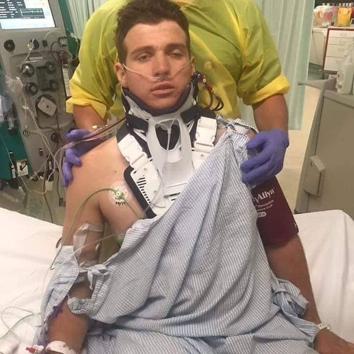 Picture of Mark Daniels in hospital, after the accident, with his neck in a brace, being held up by hospital staff