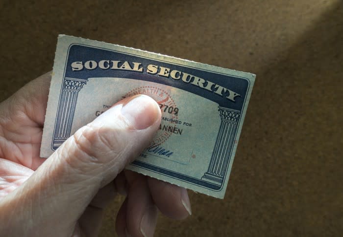 A person holding a Social Security card between their thumb and index finger.