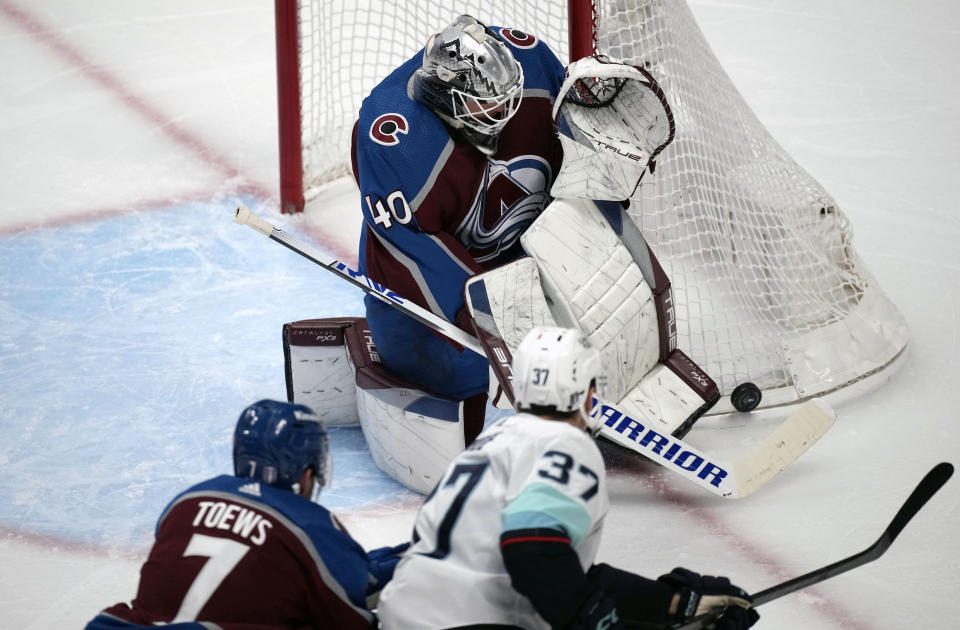 Colorado Avalanche goaltender Alexandar Georgiev, top, makes a stick-save of a shot by Seattle Kraken center Yanni Gourde, bottom right, who drives past Avalanche defenseman Devon Toews, bottom left, in the first period of Game 7 of an NHL first-round playoff series Sunday, April 30, 2023, in Denver. (AP Photo/David Zalubowski)