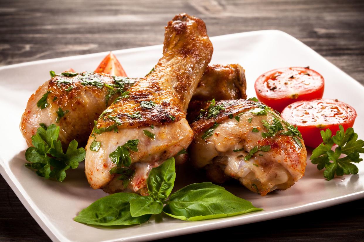 Coffee-brined chicken drumsticks on a white plate with tomato slices and herbs for garnish on a wooden table