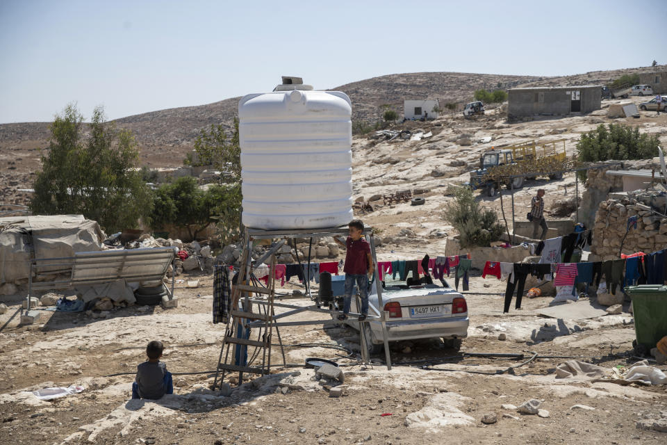 FILE - Children play by a new water tank that replaced a damaged one following a settlers' attack from nearby settlement outposts on the Palestinian Bedouin community, in the West Bank village of al-Mufagara, near Hebron, Thursday, Sept. 30, 2021. Israel’s Supreme Court has upheld a long-standing expulsion order against eight Palestinian hamlets in the occupied West Bank, potentially leaving at least 1,000 people homeless. The Israeli rights group representing the residents says the Supreme Court issued the verdict late Wednesday, May 4, 2022, when Israel was largely shut down for its Independence Day. (AP Photo/Nasser Nasser, File)