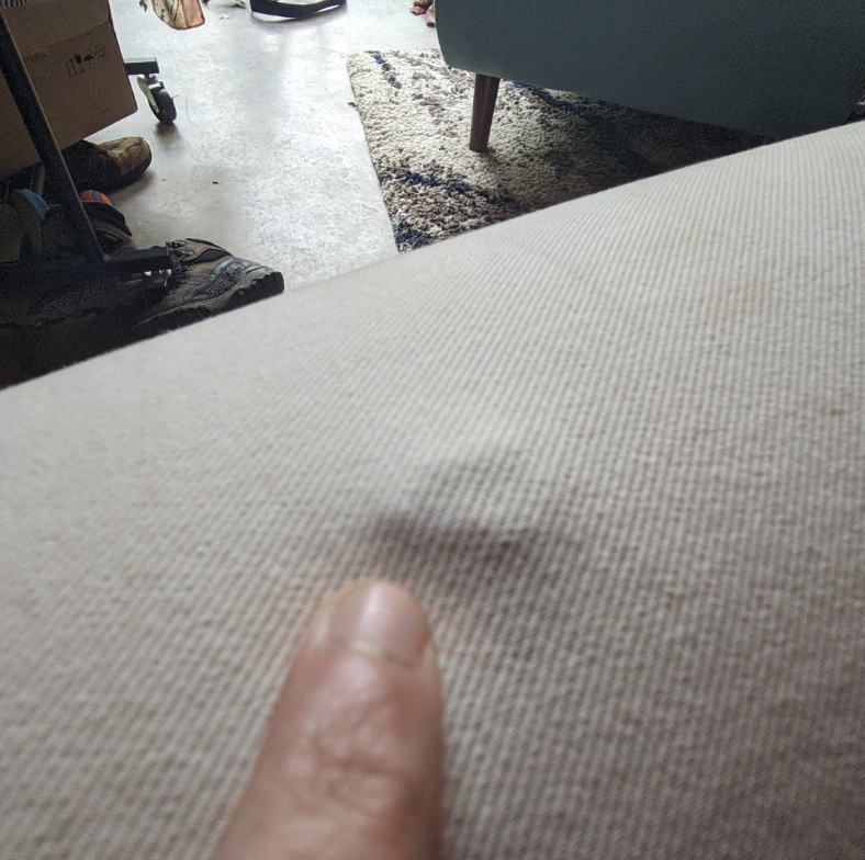A person's finger pointing at a small indentation on a fabric surface in a room with various items and furniture