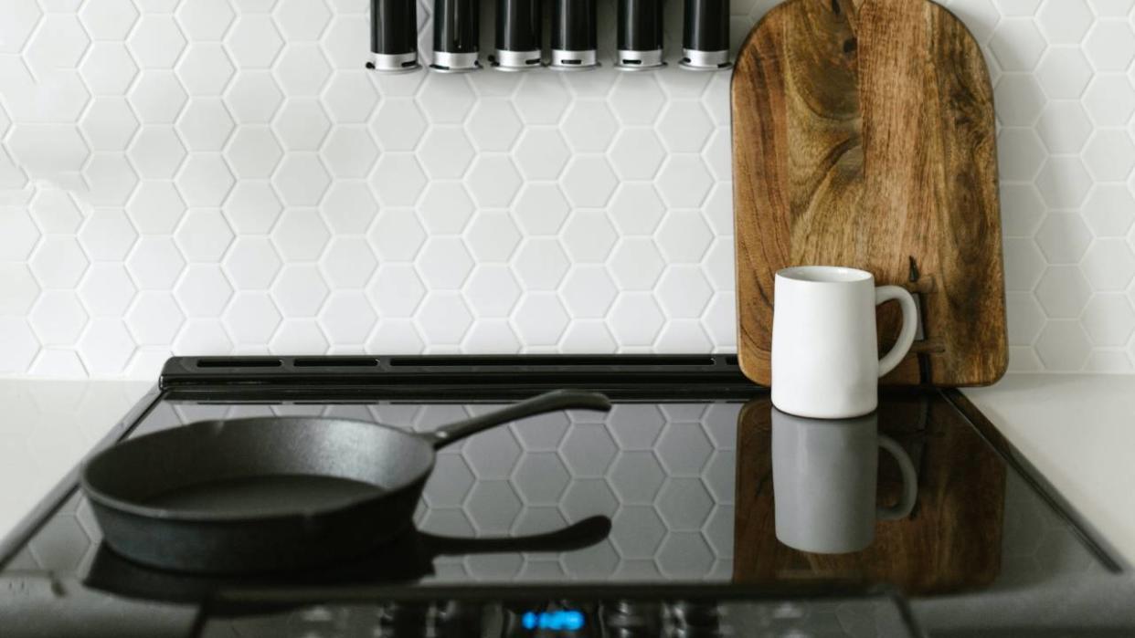  A lifestyle image of an induction hob with a saucepan, mug and chopping board resting on the surface. 