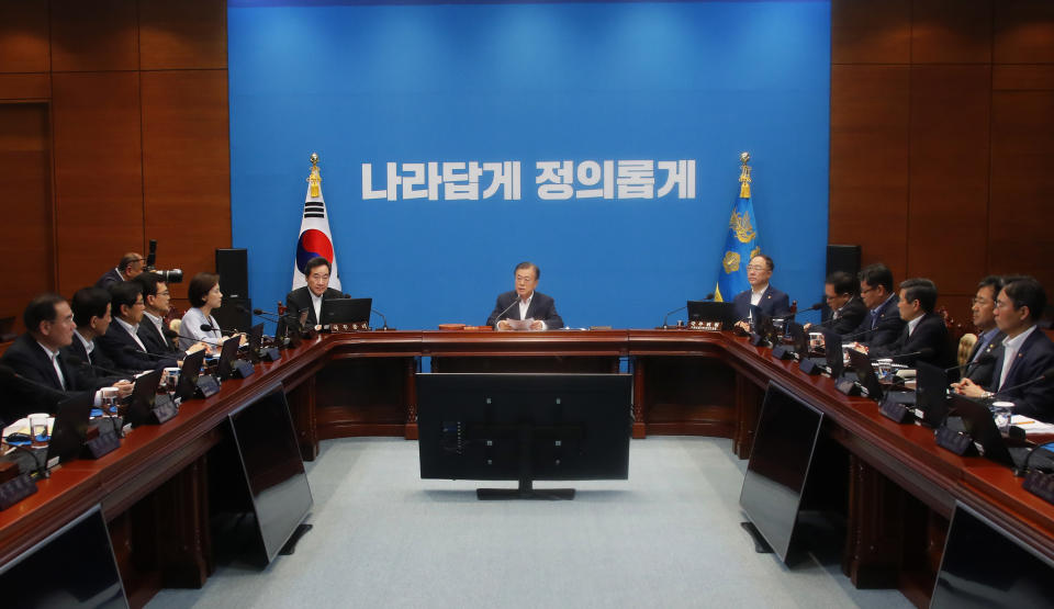 South Korean President Moon Jae-in, center, speaks during an emergency cabinet meeting at the presidential Blue House in Seoul, South Korea, Friday, Aug. 2, 2019. Moon has vowed stern countermeasures against Japan's decision to downgrade its trade status, which he described as a deliberate attempt to contain South Korea's economic growth and a "selfish" act that would damage global supply chains.The signs read: "Righteous". (Bae Jae-man/Yonhap via AP)