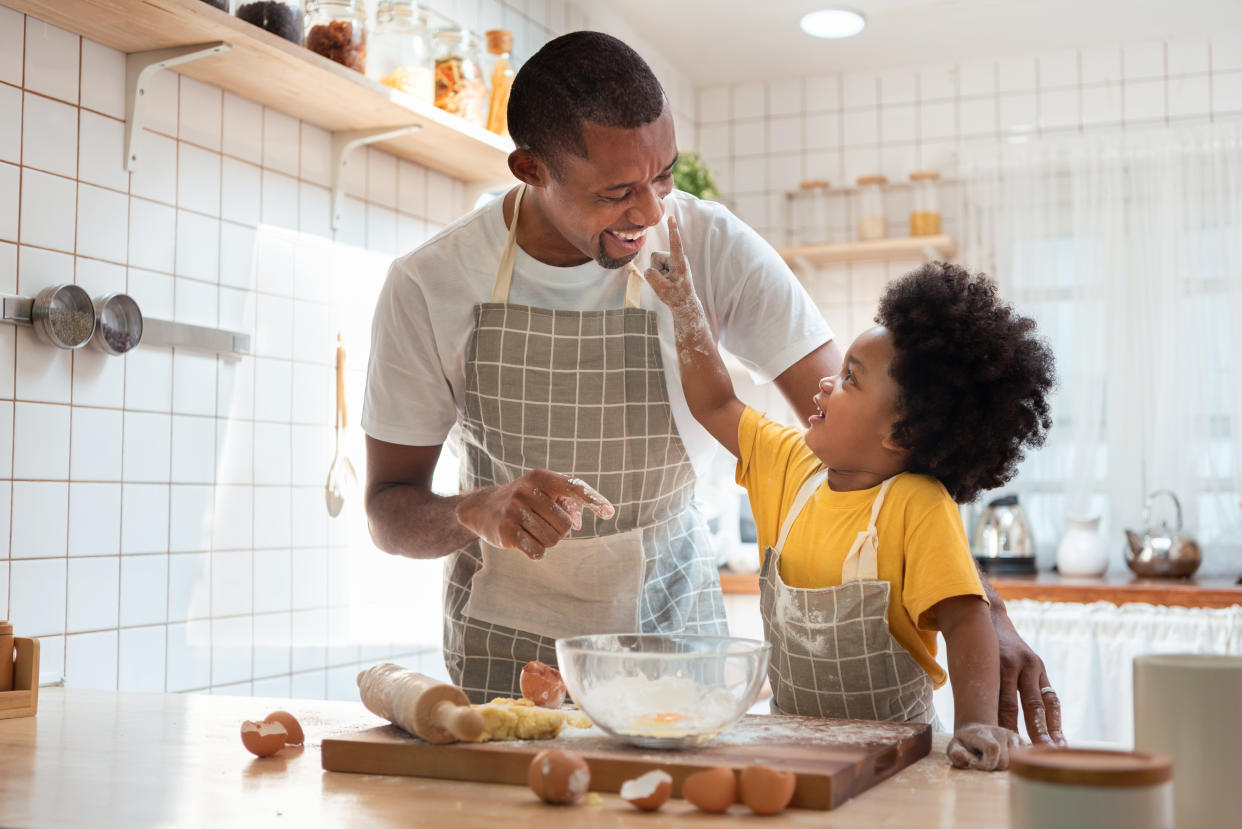 African family have fun cooking baking cake or cookie in the kitchen together, Happy smiling Black son enjoy playing and touching his father nose with finger and flour while doing bakery at home.