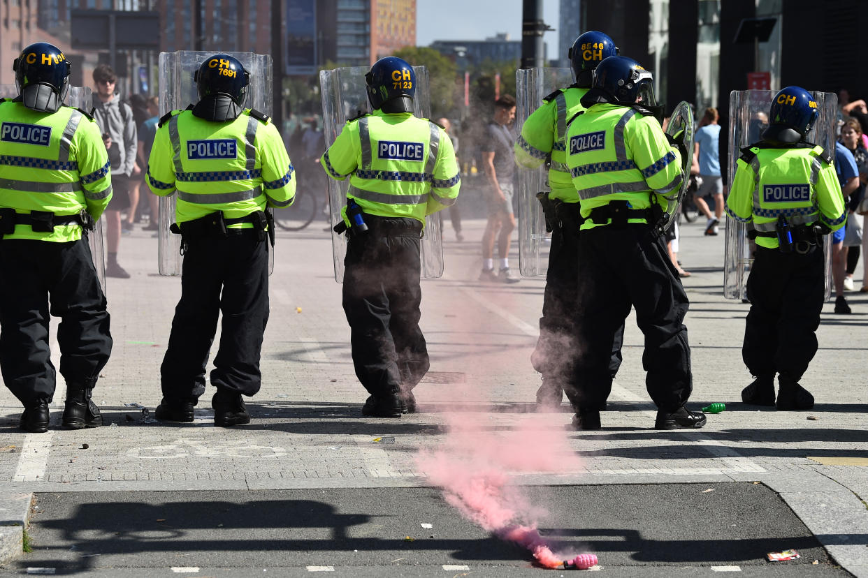 Police officers stand guard as a flare is thrown by protesters in Liverpool on August 3, 2024 during the 'Enough is Enough' demonstration held in reaction to the fatal stabbings in Southport on July 29. UK police prepared for planned far-right protests and other demonstrations this weekend, after two nights of unrest in several English towns and cities following a mass stabbing that killed three young girls. (Photo by Peter POWELL / AFP) (Photo by PETER POWELL/AFP via Getty Images)