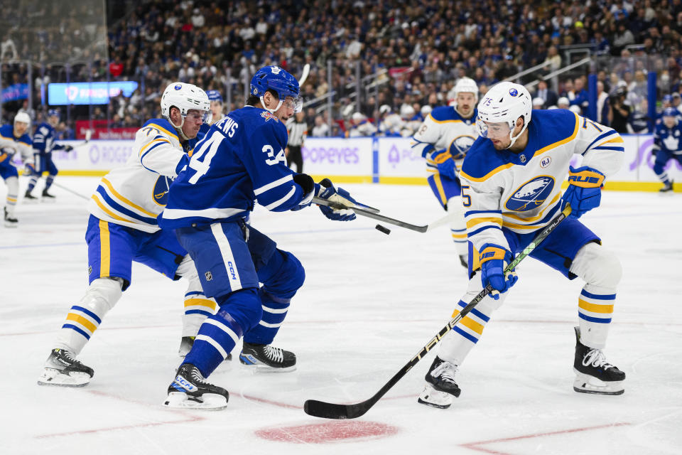 Toronto Maple Leafs center Auston Matthews (34) attacks the net while defended by Buffalo Sabres defenseman Connor Clifton (75) and left wing Victor Olofsson (71) during the second period of an NHL hockey game Saturday, Nov. 4, 2023, in Toronto. (Christopher Katsarov/The Canadian Press via AP)