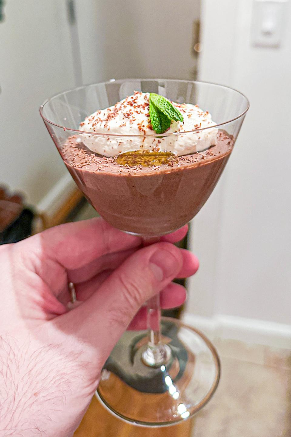 Hand holding a glass with chocolate mousse topped with whipped cream and a mint leaf