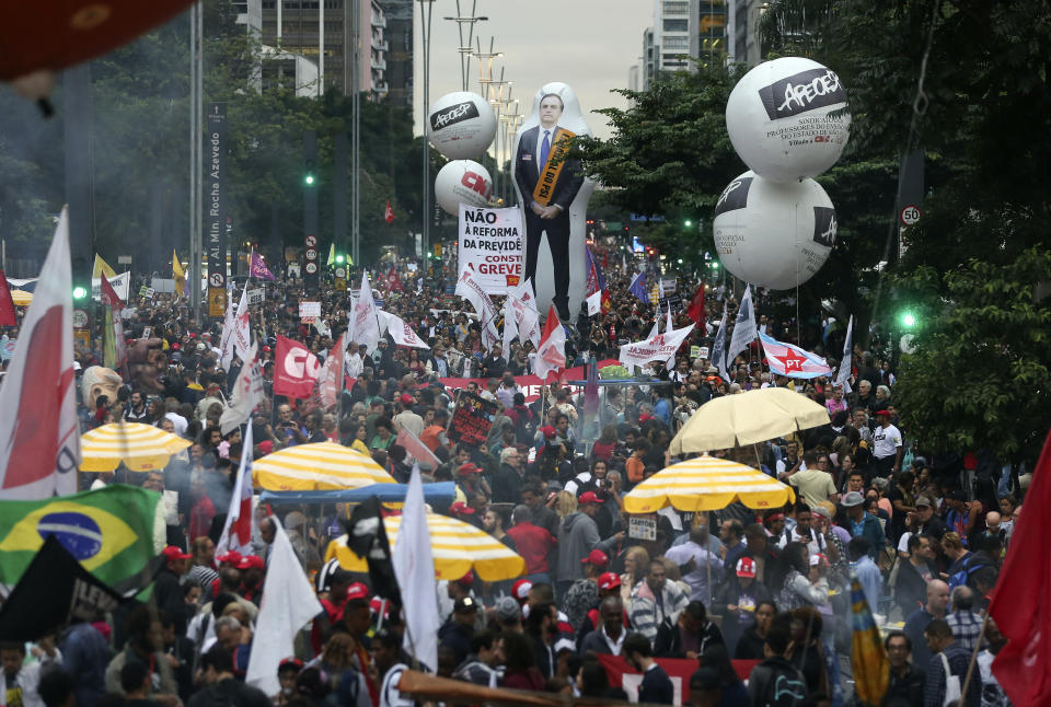 People gather, some holding a inflatable doll with the image of Brazil's president Jair Bolsonaro, during a protest against the pension reforms proposed by his government in Sao Paulo, Brazil, Friday, March 22, 2019. (AP Photo/Andre Penner)