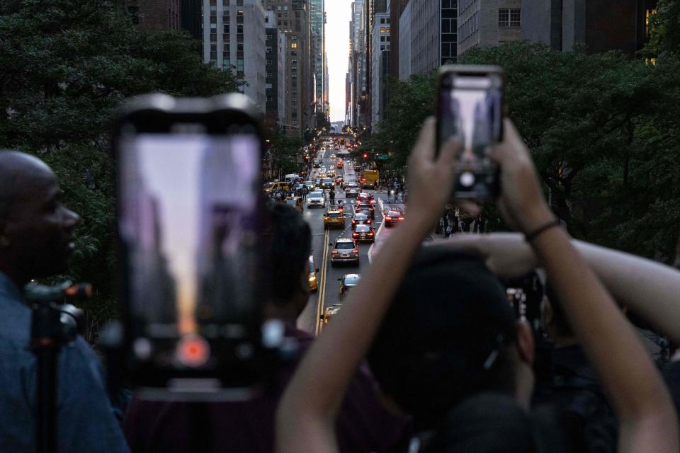 People take picture as the sun sets over Manhattan on 42nd street during the "Manhattanhenge" in New York on July 11, 2022.