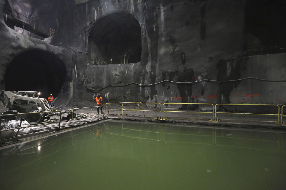 A fenced-off section of murky water with men standing on the rocky, cavelike surface next to it