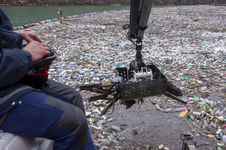 A worker operates a crane collecting waste floating in the Drina river near Visegrad, Bosnia, Wednesday, Jan. 10, 2024. Tons of waste dumped in poorly regulated riverside landfills or directly into the rivers across three Western Balkan countries end up accumulating during high water season in winter and spring, behind a trash barrier in the Drina River in eastern Bosnia. (AP Photo/Armin Durgut)