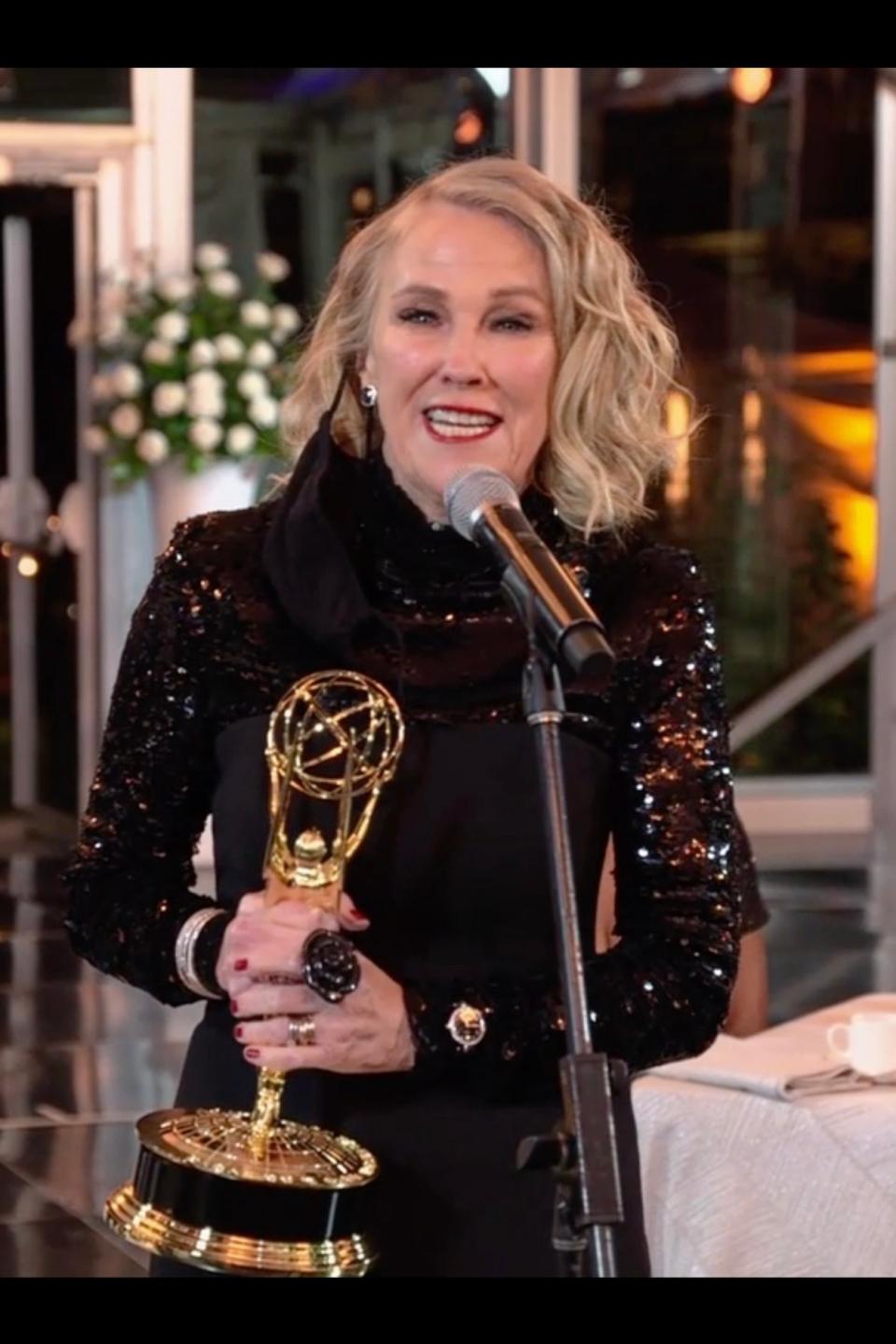 Woman in black dress holding an Emmy award at a podium with an audience in the background