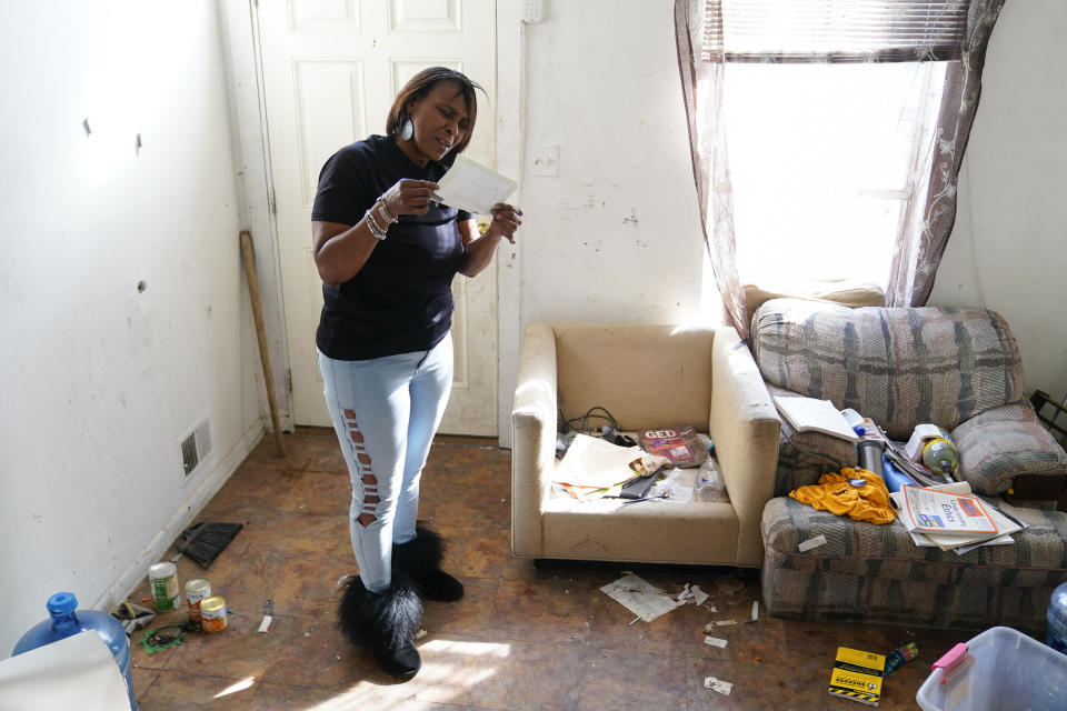 Angela Banks looks at a photograph in the unkept living room of the house she used to rent, Wednesday, Feb. 15, 2023, in Baltimore. In 2018, Banks was told by her landlord that Baltimore officials were buying her family's home of four decades, planning to demolish the three-story brick rowhouse to make room for an urban renewal project aimed at transforming their historically Black neighborhood. Banks and her children became homeless almost overnight. Banks filed a complaint Monday asking federal officials to investigate whether Baltimore's redevelopment policies are perpetuating racial segregation and violating fair housing laws by disproportionately displacing Black and low-income residents. (AP Photo/Julio Cortez)