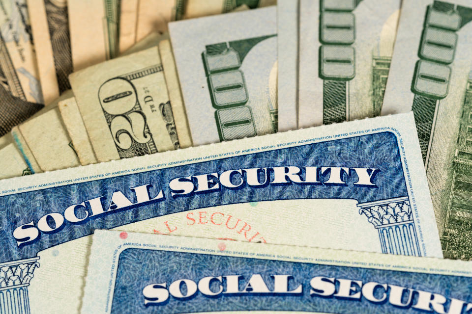 Two Social Security cards lying atop a fanned pile of cash.