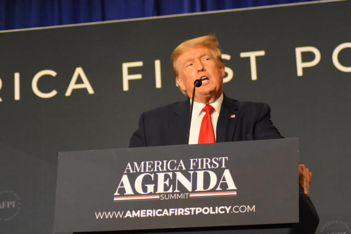 Former President Donald J. Trump at the microphone at a podium marked: America First Agenda Summit, www.americafirstpolicy.com.