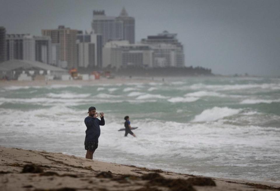 A man takes a photo of surfers and the waves during bad weather on Wednesday, Dec. 13, 2023, in South Miami Beach.