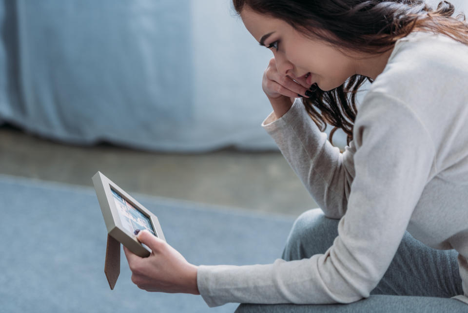 selective focus of upset woman looking at picture frame, crying and wiping tears at home