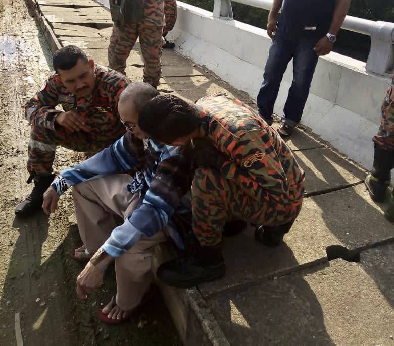 Firemen from the Pasir Gudang fire station comforting a senior citizen after he was found on the ledge of the Sungai Kim Kim bridge in Pasir Gudang today. — Picture courtesy of the Johor Fire and Rescue Department