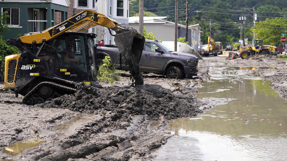 Equipment clears mud from a neighborhood as flood waters block a street, Wednesday, July 12, 2023, in Barre, Vt. Following a storm that dumped nearly two months of rain in two days, Vermonters are cleaning up from the deluge of water. (AP Photo/Charles Krupa)