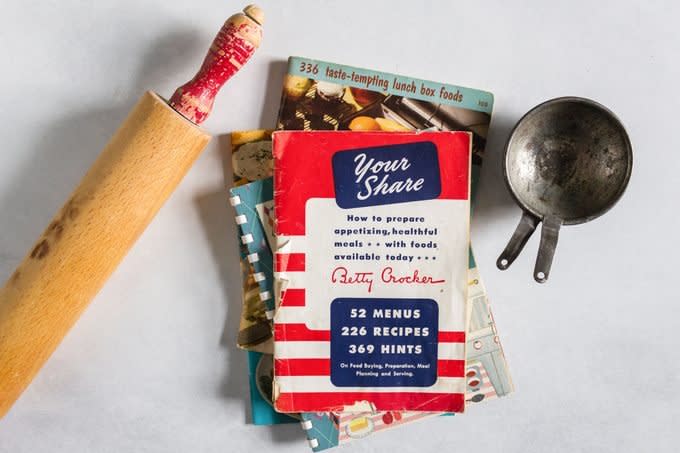 stack of vintage cookbooks with vintage rolling pin and measuring cup on marble countertop background