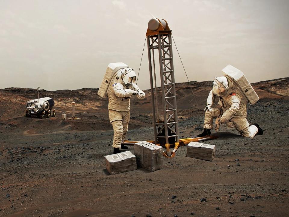 Two astronauts wearing large spacesuits conduct exercises on Mars