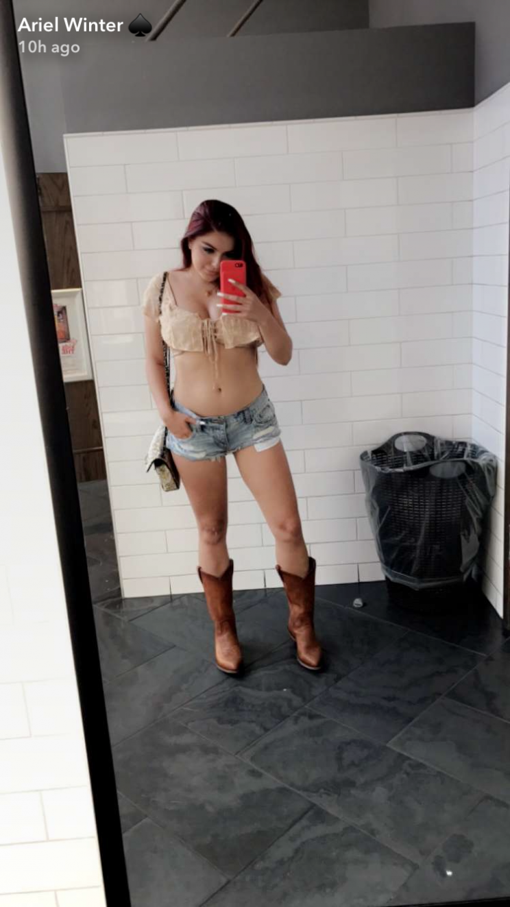 Ariel Winter in ripped denim shorts, a lace-up crop top, and cowboy boots.