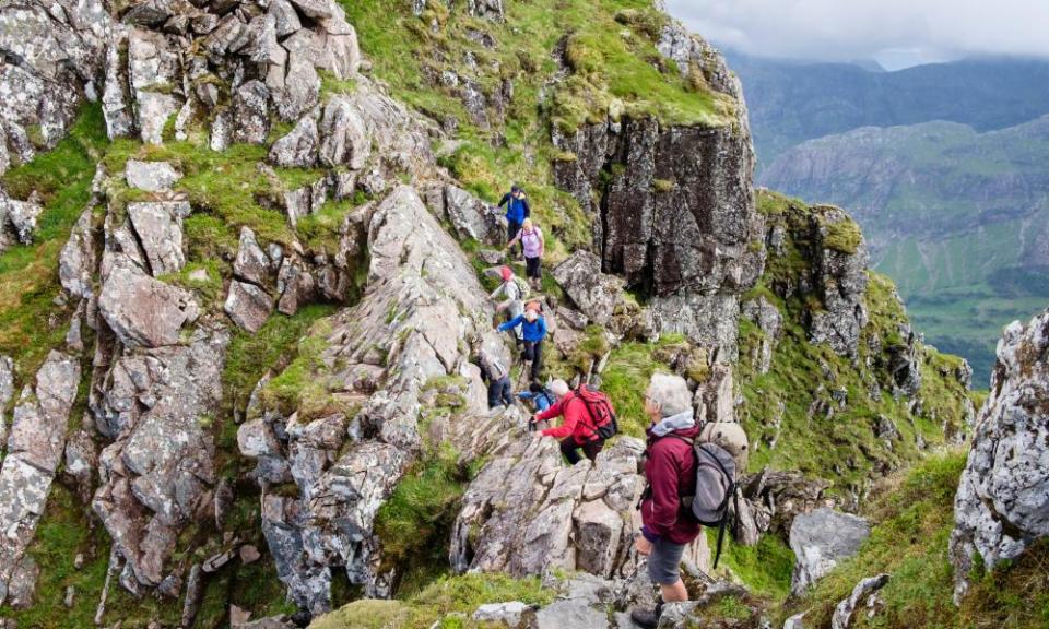 Hikers scrambling on steep rocky pinnacles of Aonach Eagach ridge