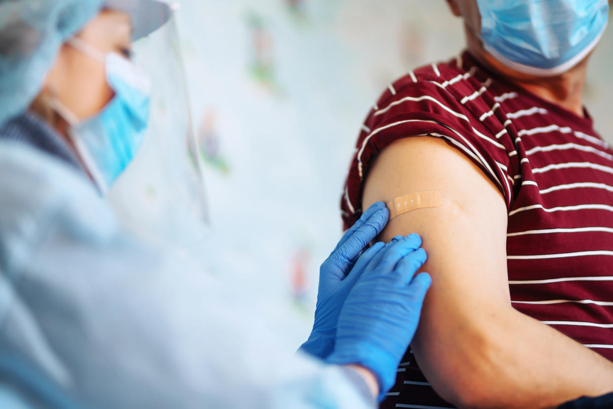 Close up photo of senior patient arm with doctor`s hands making injection. Elderly patient wearing mask to stop coronavirus spread. Covid 19 vaccination. Old people. Elderly virus protection.