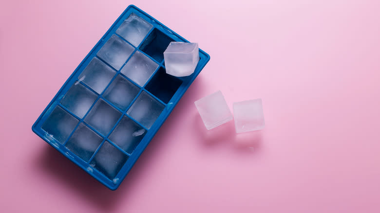 Blue Ice cube tray with three loose ice cubes on a pink background