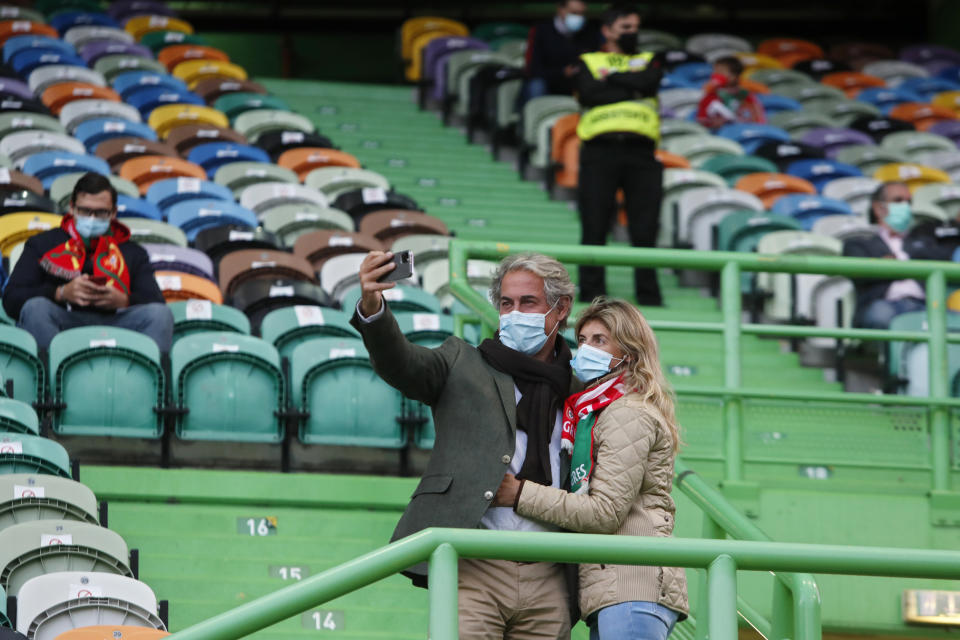 A couple wearing face masks take a selfie on the stands during a soccer match between Portugal and Sweden at the Jose Alvalade stadium in Lisbon, Portugal, Wednesday, Oct. 14, 2020. Five thousand spectators were allowed on the stands but starting Wednesday at midnight, and for the upcoming two weeks, a maximum of five people will be allowed together either indoors or outdoors in public spaces and establishments such as restaurants due to a steady increase in cases of COVID-19 in the past weeks. (AP Photo/Armando Franca)