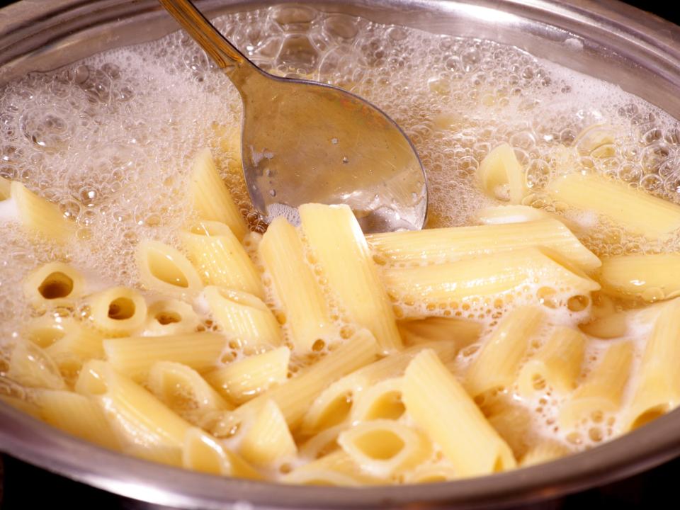 penne pasta being boiled in metal pot being stirred by metal spoon