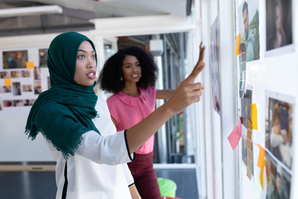 Side view of young diverse female graphic designers discussing over photographs in office. This is a casual creative start-up business office for a diverse team