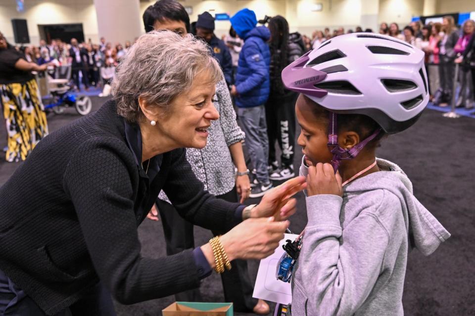 Dr. Nancy Mendelsohn, president of the ACMG Foundation, helps a young girl try on her helmet before she takes home a new, adapted bike.