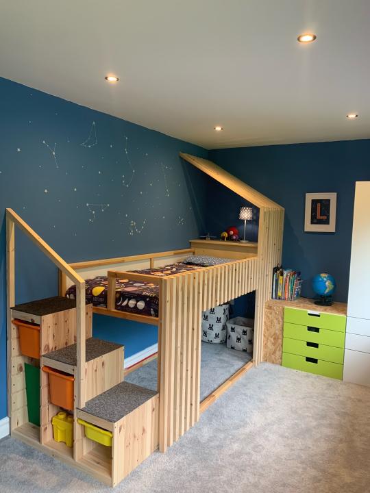 A kids bed designed in wood, with three steps and a play area underneath