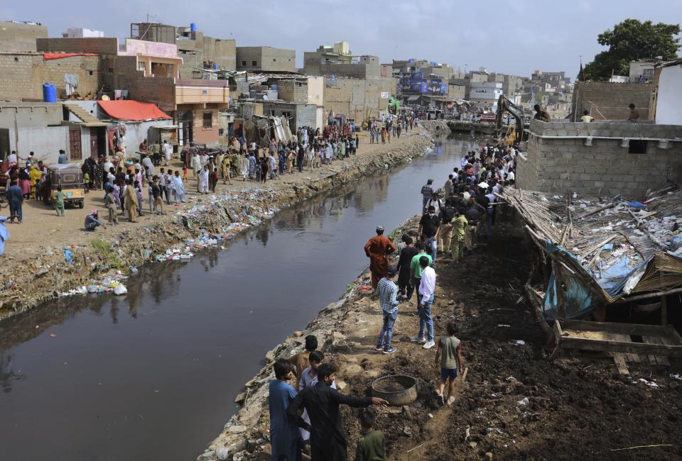 Residents watch the arrival of local authorities to demolish illegal construction alongside a drainage canal which saw flooding last week due to heavy monsoon rains, in Karachi, Pakistan, Wednesday, Sept. 2, 2020. Flash floods triggered by heavy rains killed some people and damaged scores of houses in Pakistan's scenic northwestern Swat Valley, a spokesman said Wednesday, as rescuers assisted residents in the port city of Karachi where last week's rains wreaked havoc that killed dozens. (AP Photo/Fareed Khan)