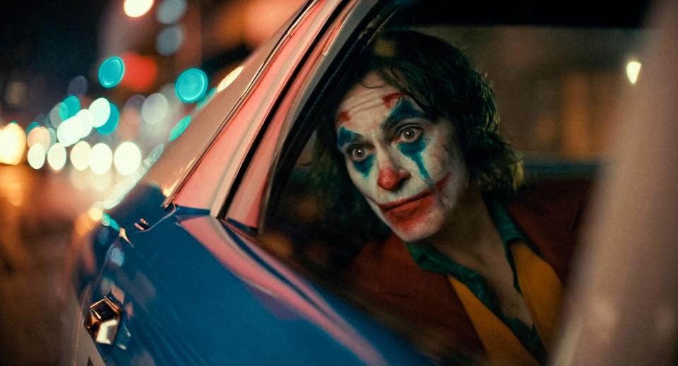 Joaquin Phoenix wears clown make-up while sitting in a cop car in "Joker"