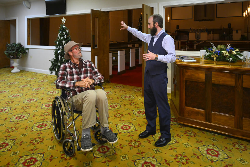 Jerry Lamb, who suffers from a spine condition, talks to Pastor Adam Kelchner at Camden First United Methodist Church Thursday, Dec. 8, 2022, in Camden, Tenn. The church at the urging of the pastor recently had a couple pews cut in half so Jerry, and anyone else who uses a wheelchair, walker or other aid, can still sit with the rest of the congregation. (AP Photo/John Amis)