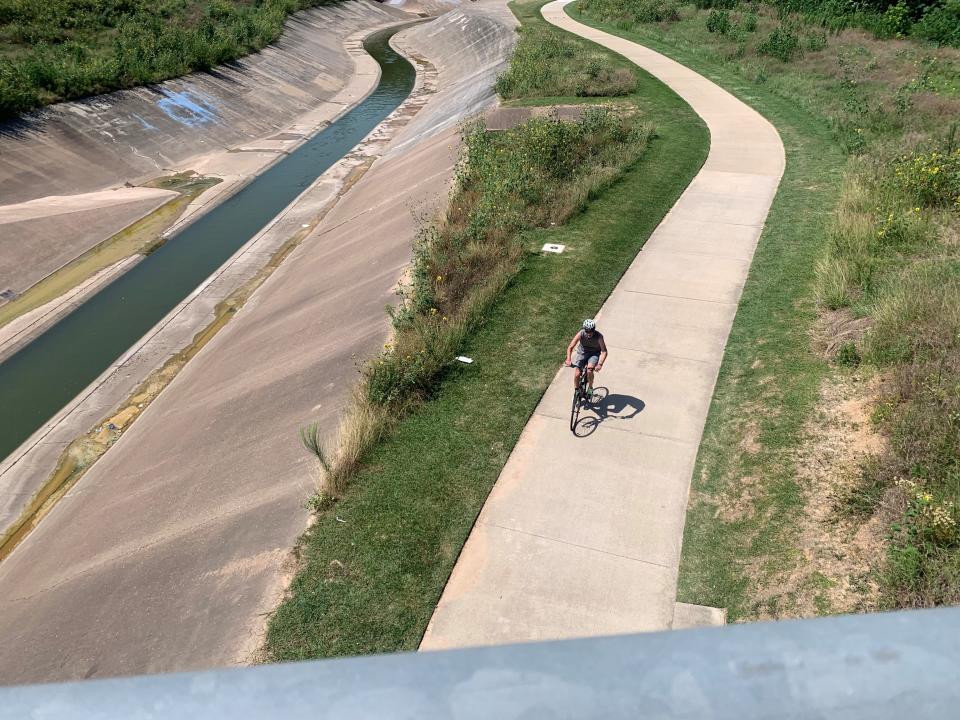 A bicyclist rides alongside the bayou drainage area toward a pedestrian overpass connecting The Heights to the Sawyer Yards area near Bayou Greenways Park June 19, 2023, in Houston.