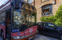 A group of people wave from a window as a bus delivers a loudspeaker message from family and friends in Brussels, Wednesday, April 22, 2020. With streets in the Brussels capital mostly devoid of loud traffic and honking horns, a simple piece of emotional poetry can split the air. The public bus company, STIB-MIVB, has been calling on people to send in voice messages, which are now delivered by a special bus driving in a loop to connect all the messages and leave a trail of happiness. (AP Photo/Olivier Matthys)