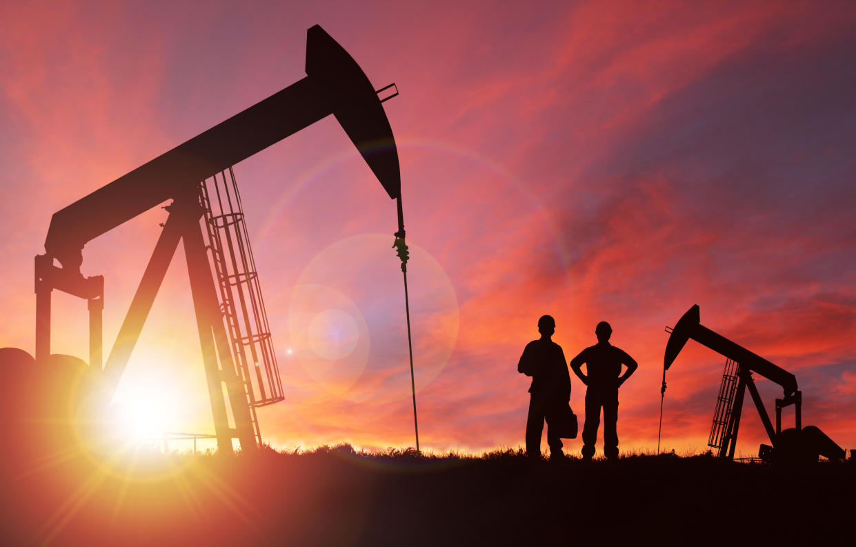 Pump jack silhouette and hard hat workers against a sunset sky with deliberate lens flare and copy space. These jacks can extract between 5 to 40 liters of crude oil and water emulsion at each stroke.