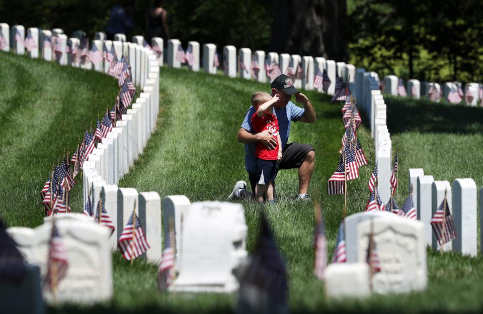 Tony Wilson, right, showed his grandson Liam Wilson, 3, how to salute a grave marker on Memorial Day at the Cave Hill National Cemetery in Louisville, Ky. on May 30, 2022.  Coincidentally, Liam stopped at a marker of a soldier named Wilson as well.