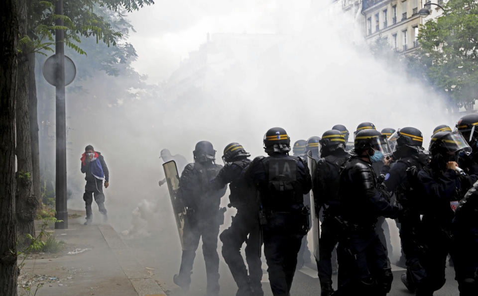 A protestor covers their face against gas canisters as police move their line during a demonstration in Paris, France, Saturday, July 31, 2021. Demonstrators gathered in several cities in France on Saturday to protest against the COVID-19 pass, which grants vaccinated individuals greater ease of access to venues. (AP Photo/Adrienne Surprenant)