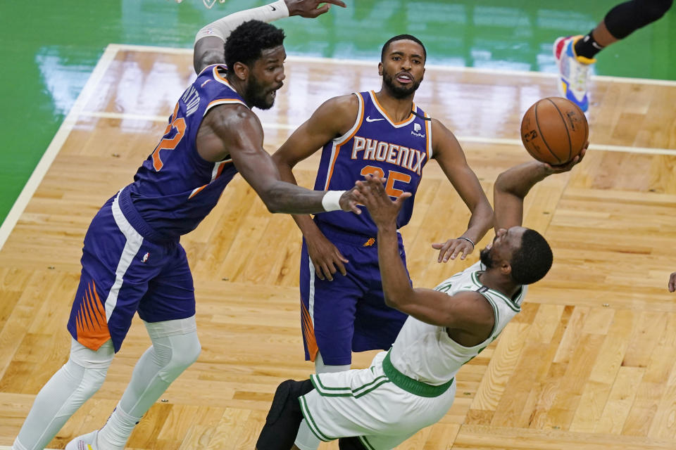 Boston Celtics guard Kemba Walker shoots and scores while falling backward, next to the defense of Phoenix Suns center Deandre Ayton (22) and forward Mikal Bridges (25) in the second half of an NBA basketball game Thursday, April 22, 2021, in Boston. (AP Photo/Elise Amendola)