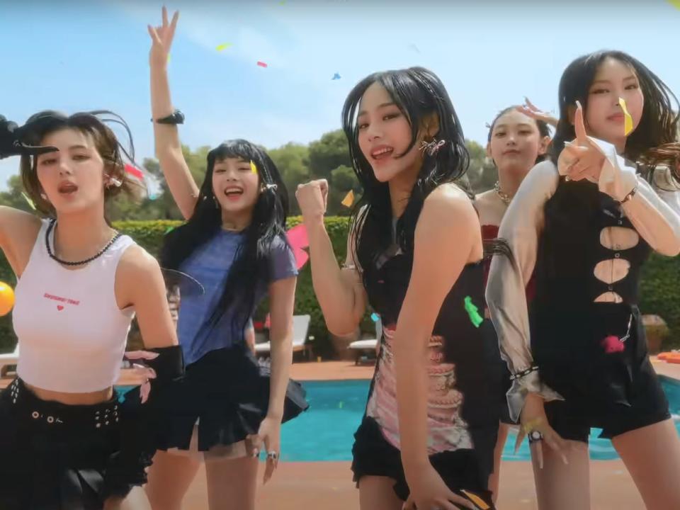 the five members of newjeans in the music video for ETA, dancing together, flashing piece signs, and smiling near a pool