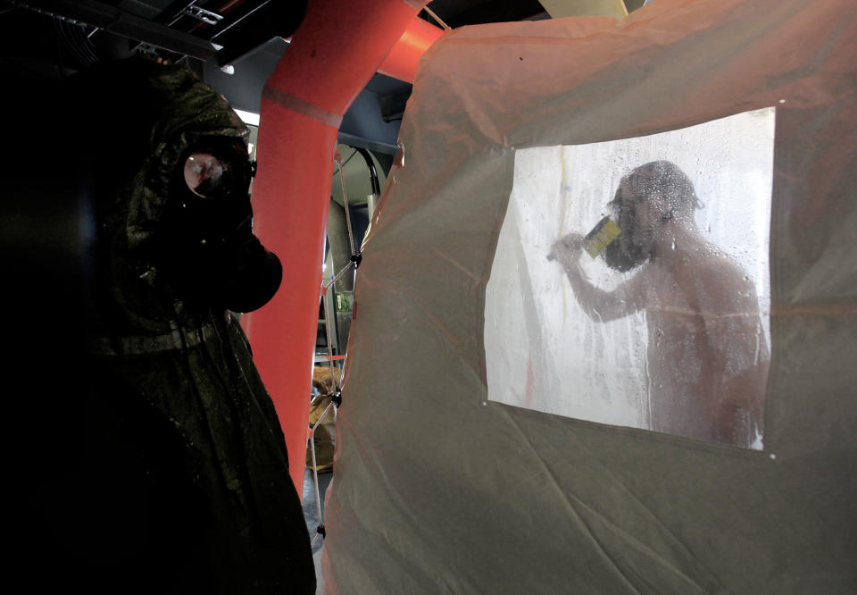 A crew member of the Danish warship Esbern Snare enters a decontamination shower wearing a gas mask, while another crew member waits, during drills at sea between Cyprus and Syria, Sunday, Jan. 5, 2014. Two cargo ships and their warship escorts set sail at waters near Syria where they will wait for orders on when they can head to the Syrian port of Latakia to pick up more than 1,000 tons of chemical agents. (AP Photo/Petros Karadjias)